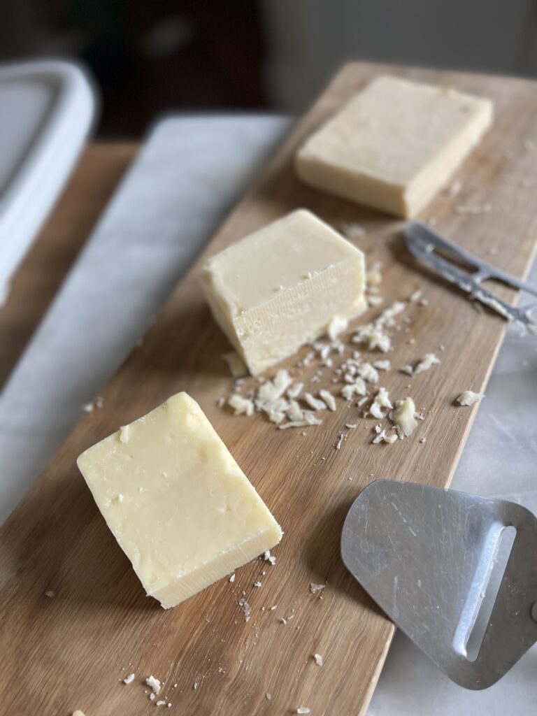 Three Cabot cheddar cheeses at different age profiles (3 year, 5 year, and 10 year) sitting on a wooden board.